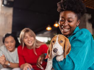 Black woman socializing her Beagle puppy during a social gathering with female friends