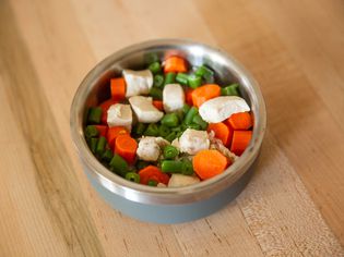 Metal dog bowl filled with homemade puppy food on wooden surface