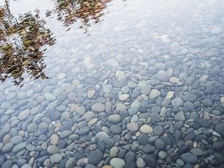 Pebbles on a river bed. Reflections and ripples on the surface.
