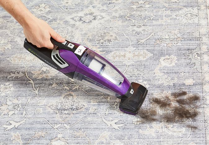 Person using Bissell Pet Hair Eraser Cordless Handheld Vacuum to clean fur from carpet