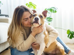 Woman sitting on floor hugging pit bull dog